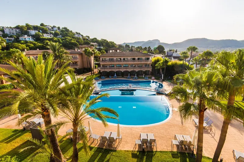 Vue aérienne d'une piscine d'hôtel entourée de palmiers et de bâtiments.
