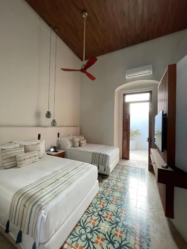 Chambre lumineuse avec deux lits et carrelage décoratif.