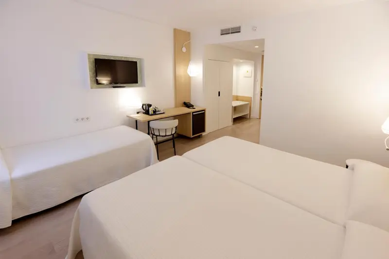 Chambre lumineuse avec lits simples et bureau.