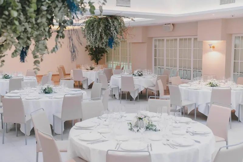 Une salle lumineuse est mise en scène pour un banquet avec des tables rondes nappées et des arrangements floraux.