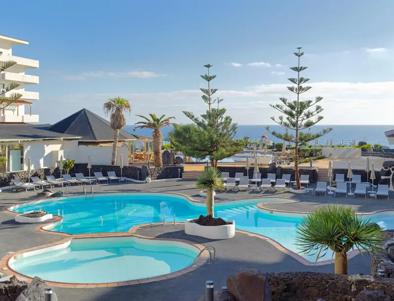 Piscine extérieure d'un complexe hôtelier ensoleillé avec chaises longues et végétation tropicale.