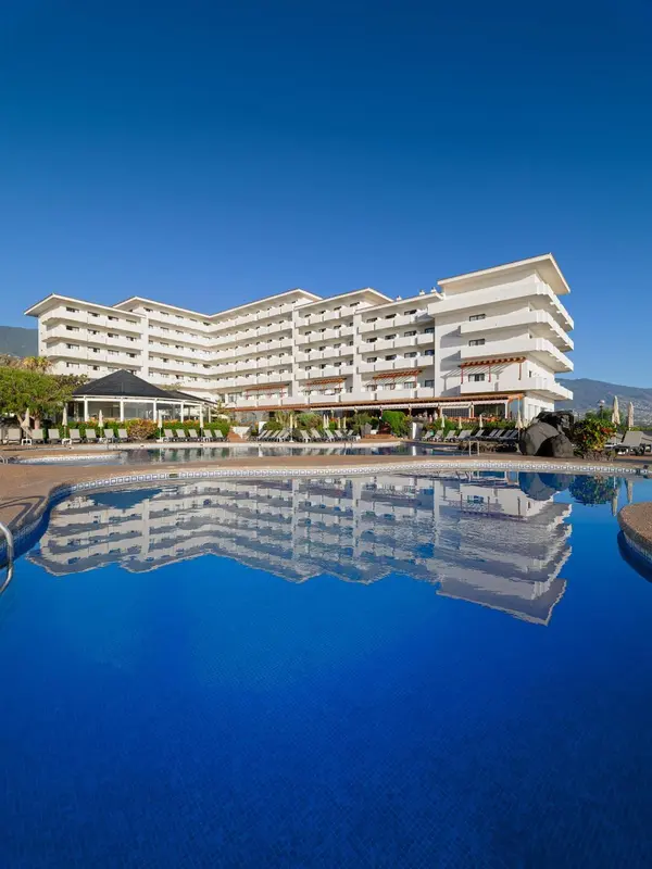 Bâtiment blanc à plusieurs étages reflété dans une piscine bleu clair.