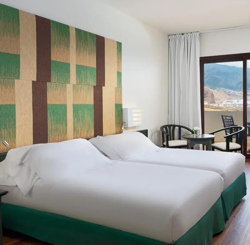 Une chambre lumineuse avec un grand lit et un coin salon donnant sur une vue dégagée.