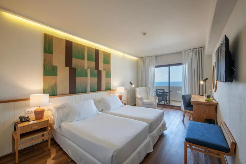Chambre lumineuse avec deux lits simples et vue sur la mer.