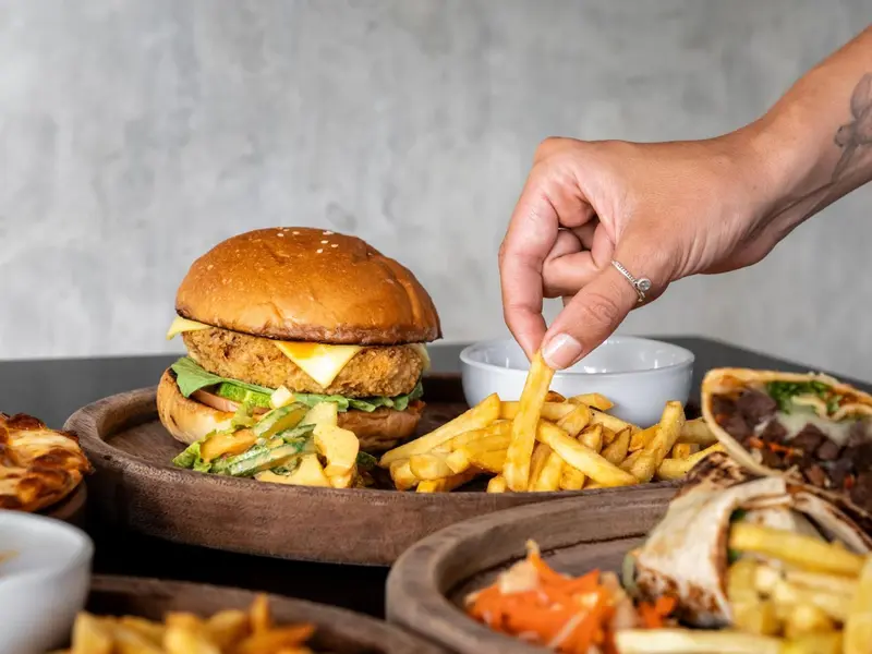 Une main prend une frite parmi une assiette de frites, un hamburger et un wrap.