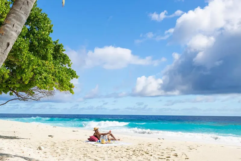 Une plage de sable blanc bordée d'eau turquoise sous un ciel nuageux.