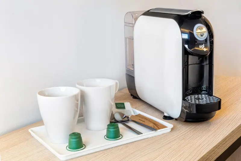 Une cafetière avec tasses et dosettes sur un plateau en bois.