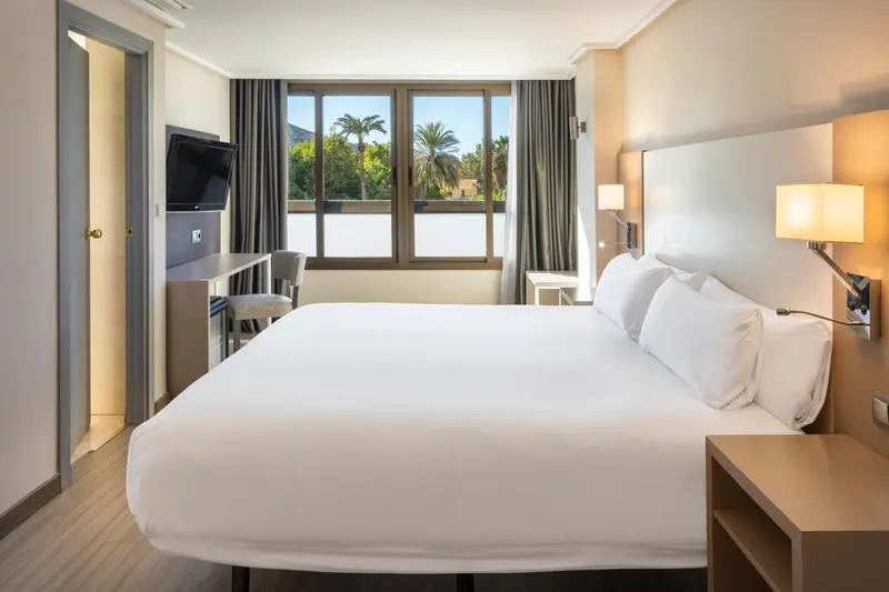 Une chambre d'hôtel lumineuse avec un grand lit et une vue sur la végétation.
