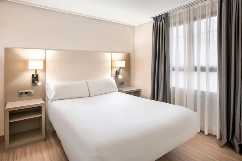 Une chambre lumineuse avec un grand lit recouvert d'une couette blanche.