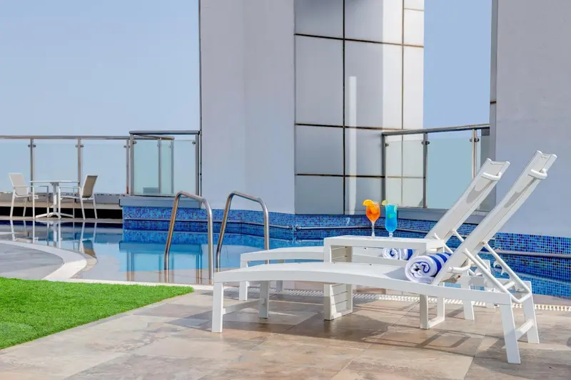 Transats blancs au bord d'une piscine avec des cocktails et une pelouse verte.