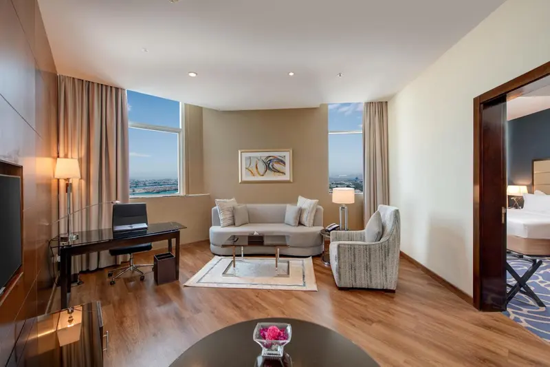 Un salon lumineux avec canapé, fauteuil et bureau donnant sur une vue urbaine.