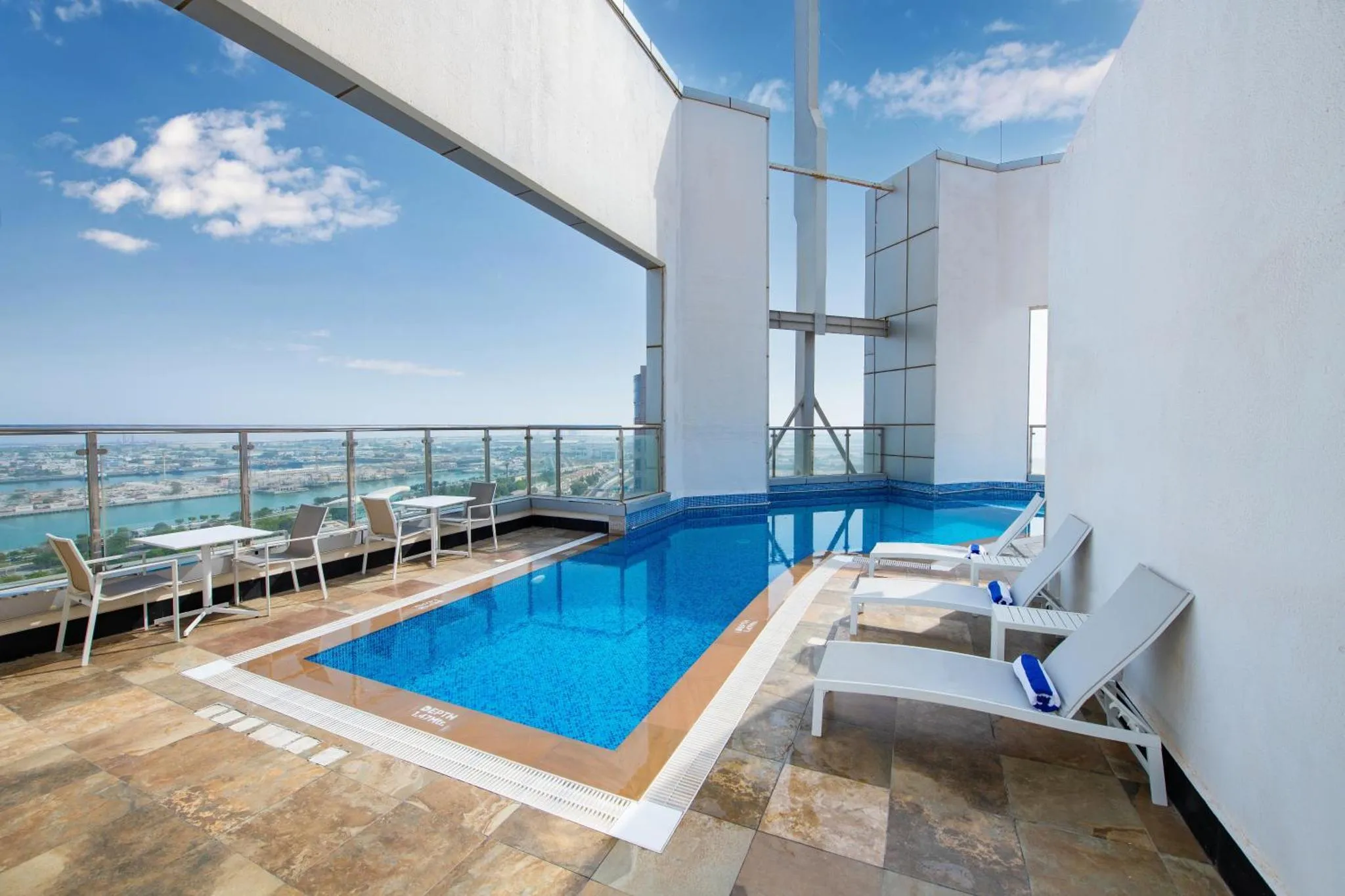 Terrasse avec piscine et mobilier de détente offrant une vue sur la ville et la mer.