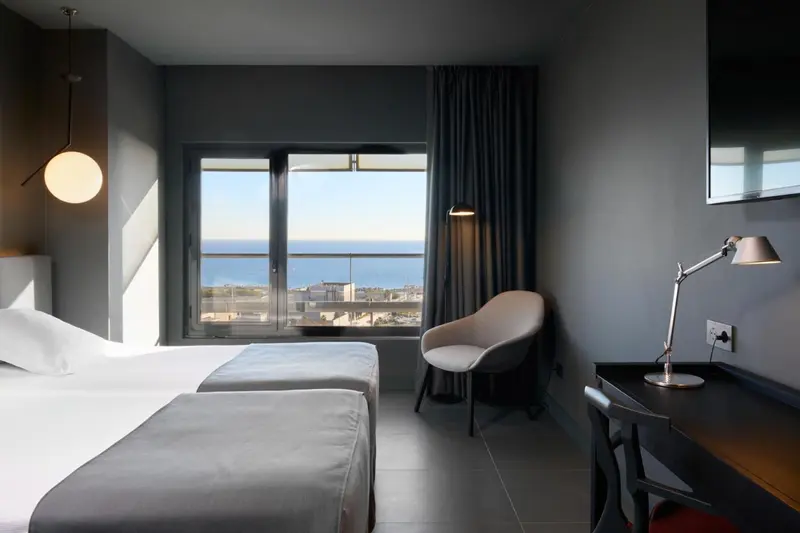 Chambre lumineuse avec vue sur la mer et un coin lecture.