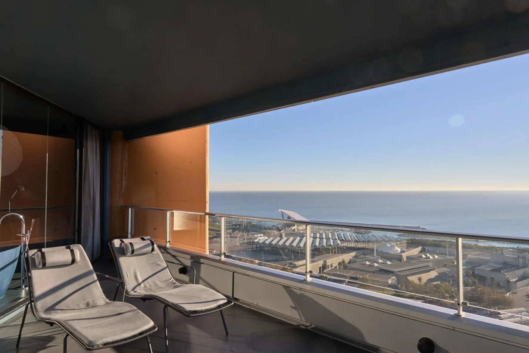 Deux fauteuils de relaxation sur une terrasse avec vue sur la mer et un aéroport.