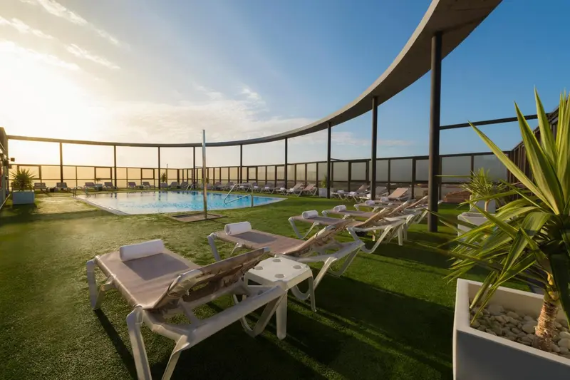 Transats blancs disposés autour d'une piscine rectangulaire sur une terrasse en gazon synthétique.