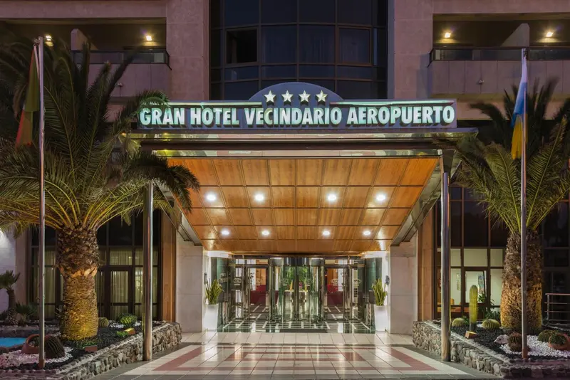 Façade d'un grand hôtel illuminé avec des palmiers et une entrée imposante.