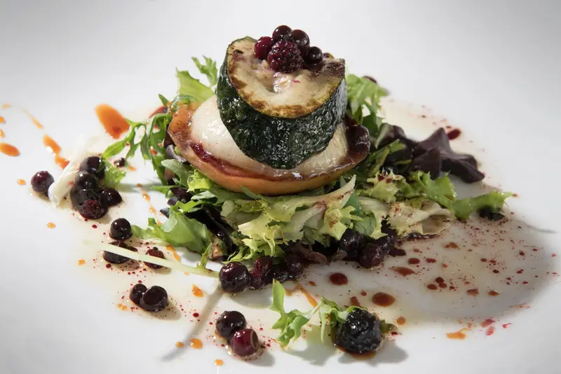 Assiette raffinée composée de légumes et de fruits rouges, présentée avec une sauce colorée.