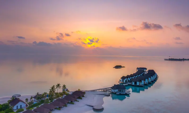 Cabanes sur pilotis au coucher du soleil sur une eau calme.