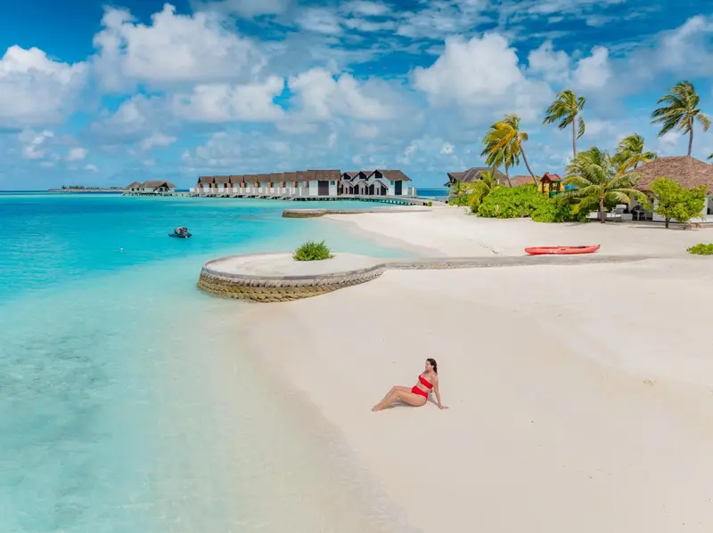 Plage de sable blanc bordée d'eau turquoise et de végétation tropicale.