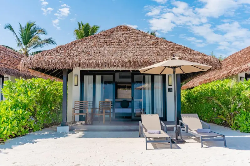 Une terrasse ensoleillée devant un bungalow à toit de chaume.