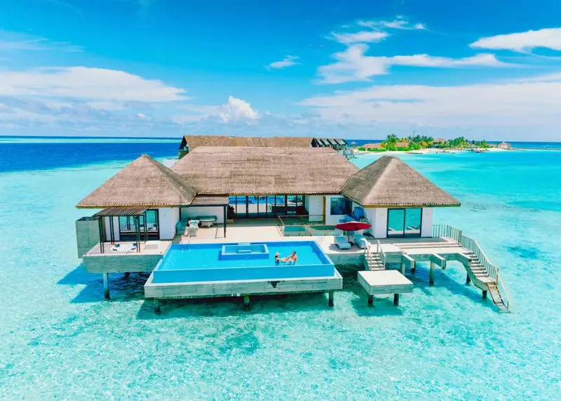 Vue aérienne d'une villa sur pilotis avec piscine privée et accès à une plage turquoise.