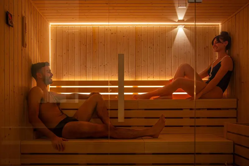 Deux personnes se détendent sur des bancs en bois dans un sauna lumineux.