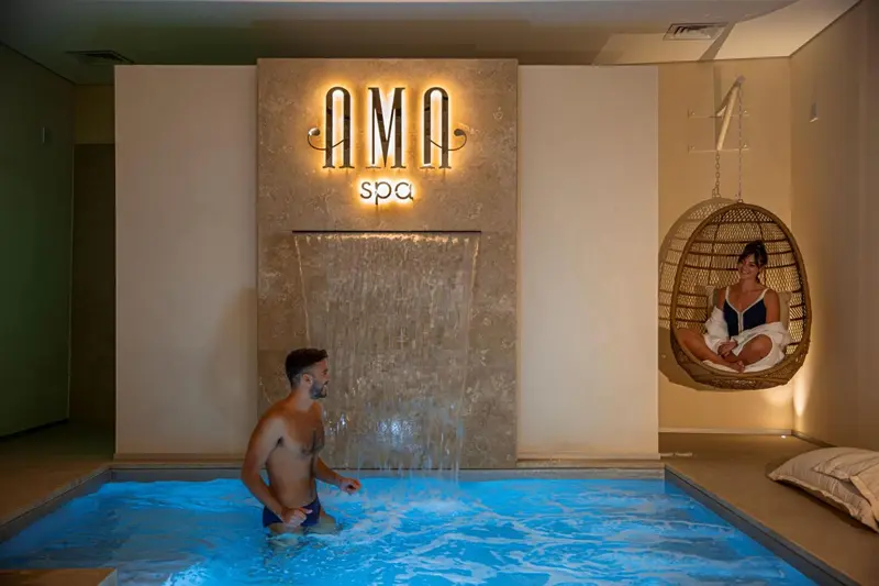Un homme sort d'une piscine intérieure tandis qu'une femme se détend dans un fauteuil suspendu.