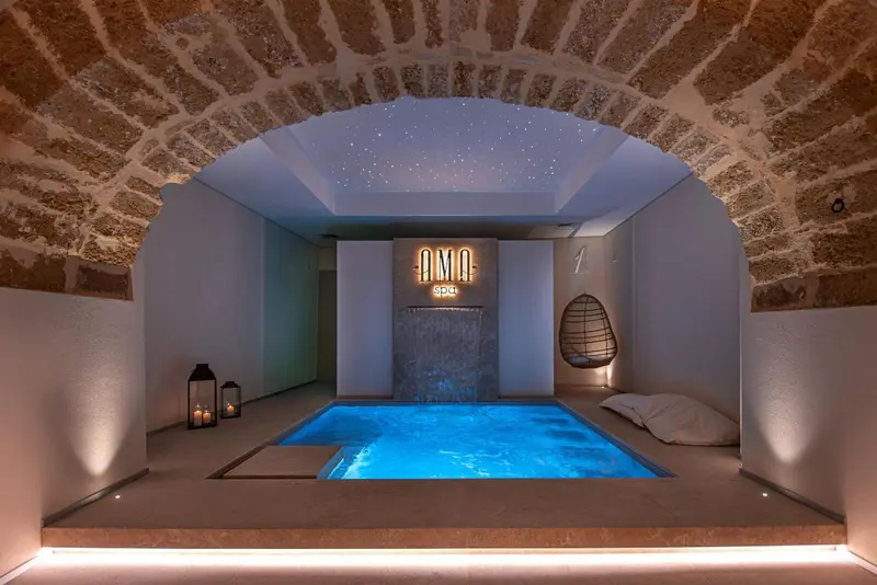 Une petite piscine intérieure éclairée dans un espace voûté en pierre.