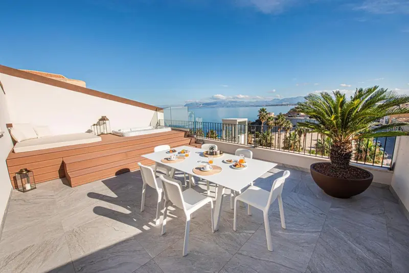 Une table à manger est mise en scène sur une terrasse ensoleillée avec vue sur la mer.