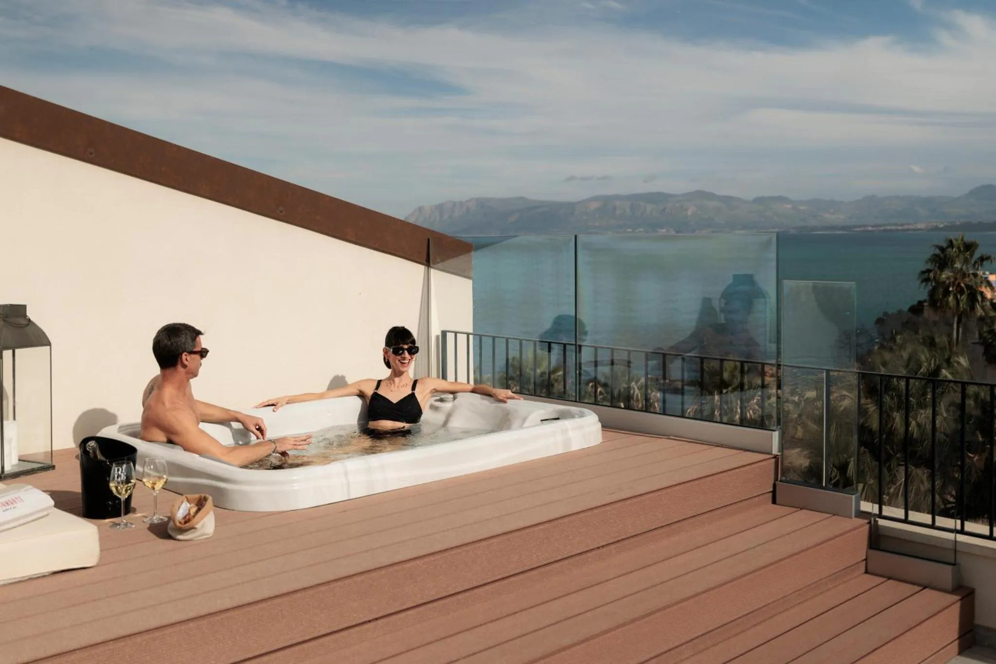 Deux personnes se détendent dans un jacuzzi sur une terrasse avec vue sur la mer.