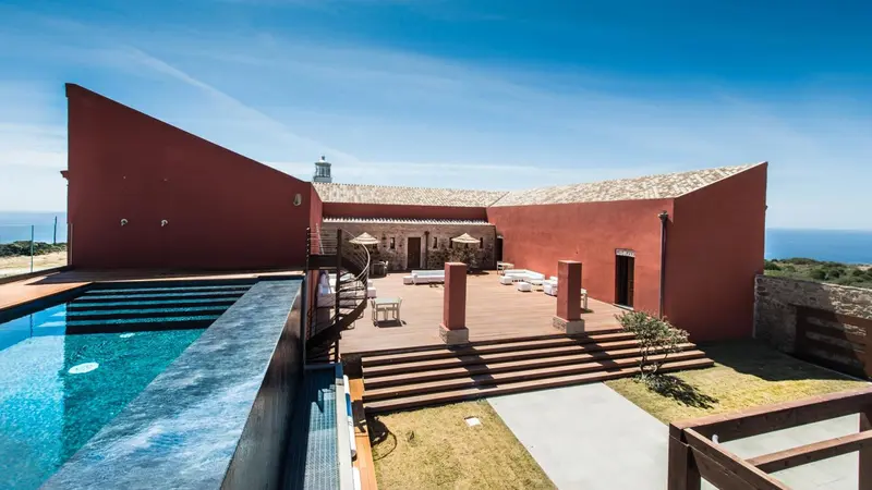 Bâtiment rouge et piscine à débordement avec vue sur la mer.