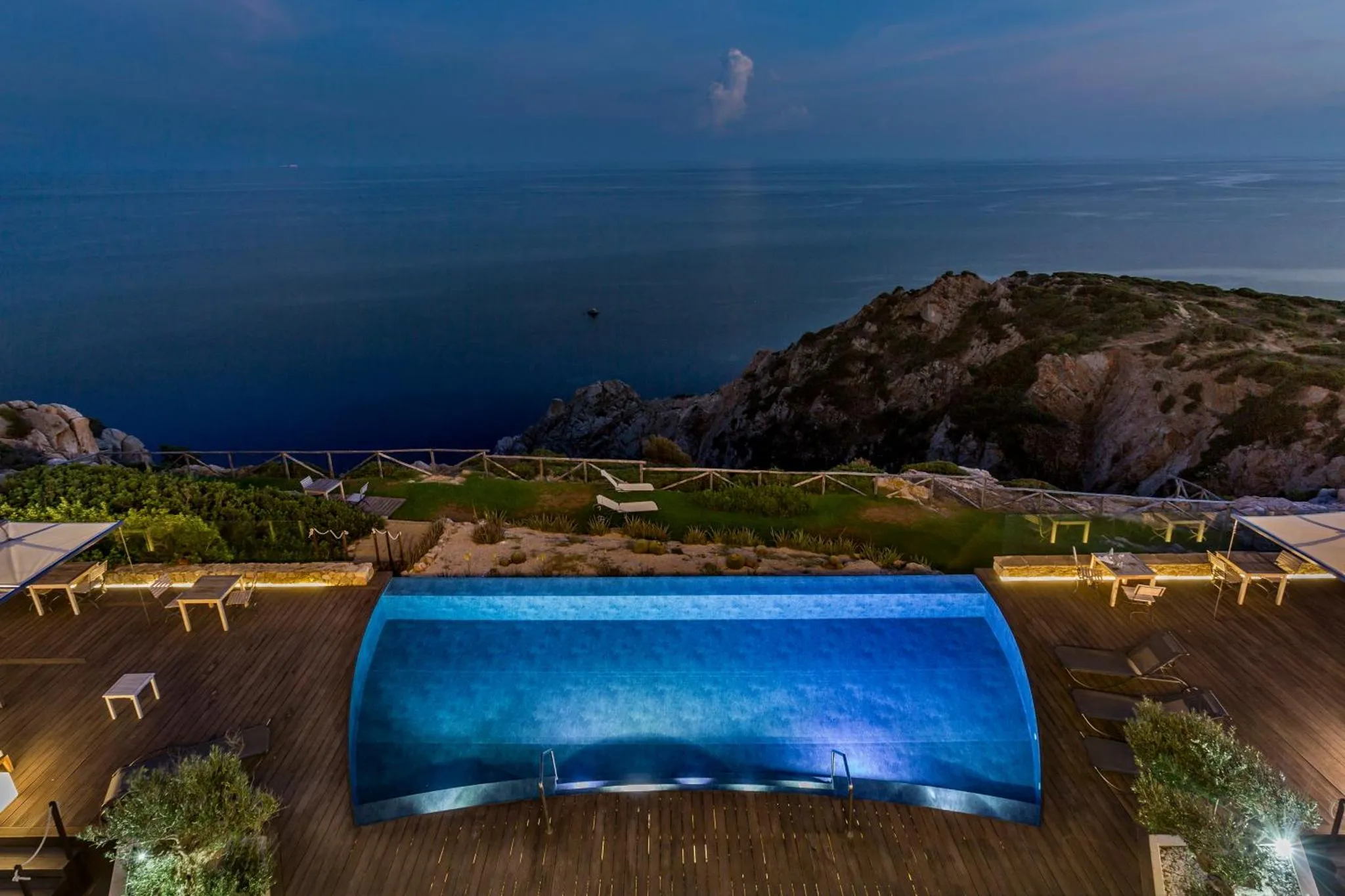 Une piscine à débordement illuminée surplombe la mer au crépuscule.