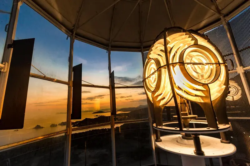 Vue intérieure d'un phare illuminé au coucher du soleil sur une côte montagneuse.
