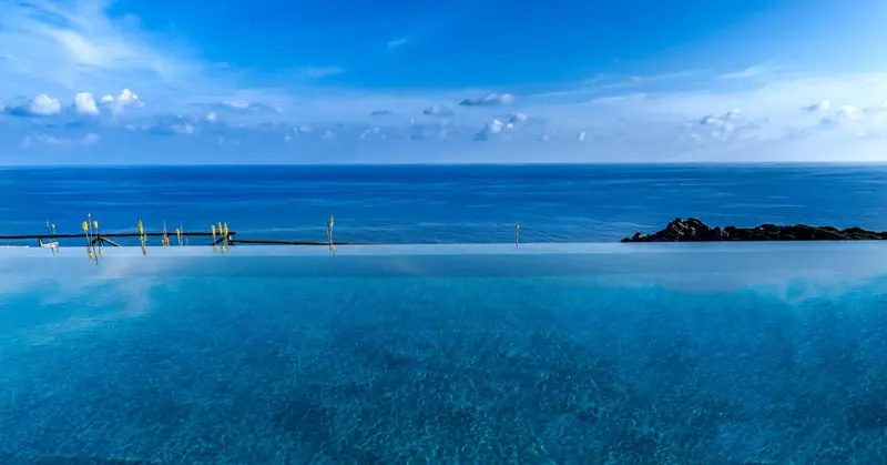 Vue d'une piscine à débordement sur l'océan sous un ciel nuageux.