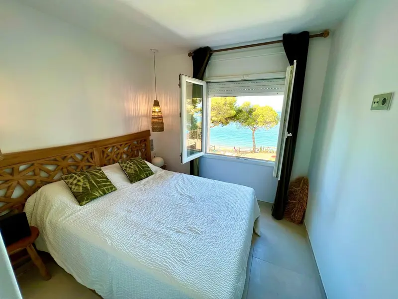 Une chambre lumineuse avec un lit fait et une vue sur la mer par la fenêtre.