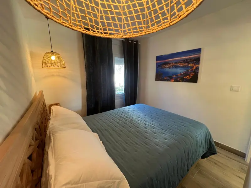 Une chambre lumineuse avec un grand lit recouvert d'une couette verte et une décoration murale représentant un paysage côtier.