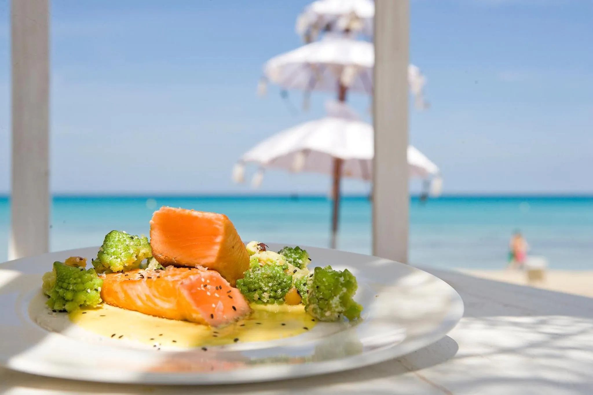 Assiette de poisson et de légumes servis sur une terrasse ensoleillée face à la mer.