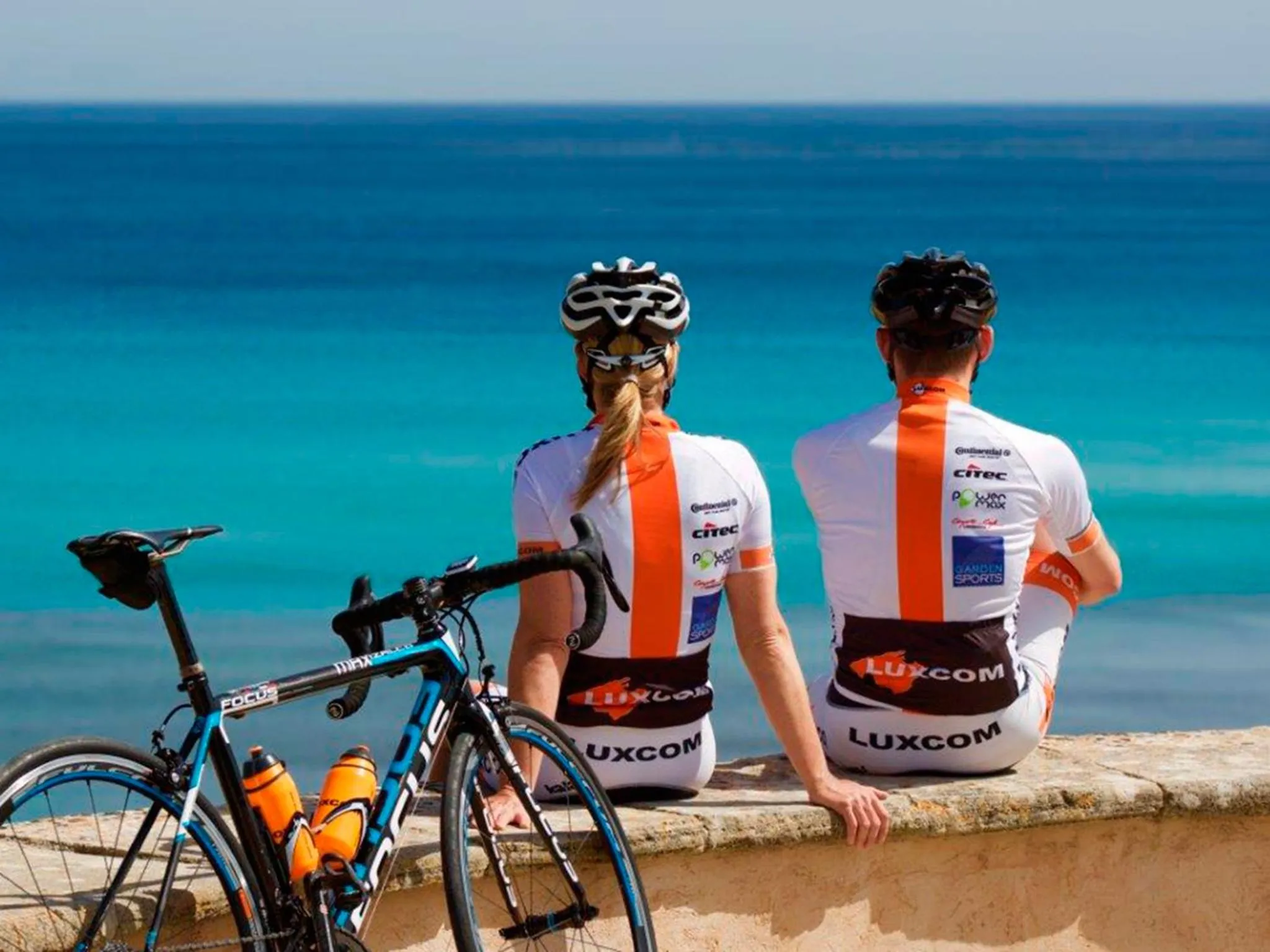 Un couple de cyclistes est assis sur un muret face à la mer.
