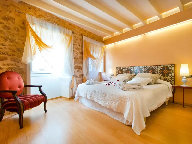 Une chambre lumineuse avec un lit à baldaquin et un fauteuil rouge.