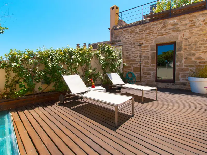 Deux transats blancs invitent à la détente sur une terrasse en bois près d'une piscine.