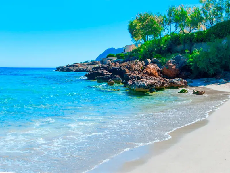 Une plage de sable blanc bordée d'une eau turquoise et de rochers.