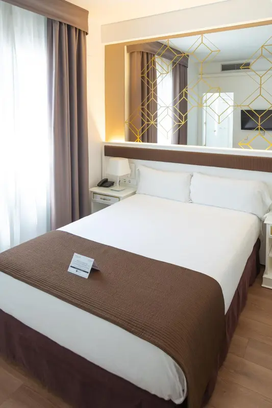 Une chambre d'hôtel lumineuse avec un grand lit recouvert d'une courtepointe.