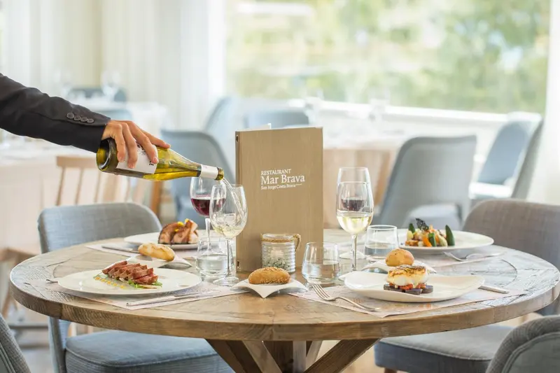 Un serveur verse du vin à table dans une salle lumineuse.