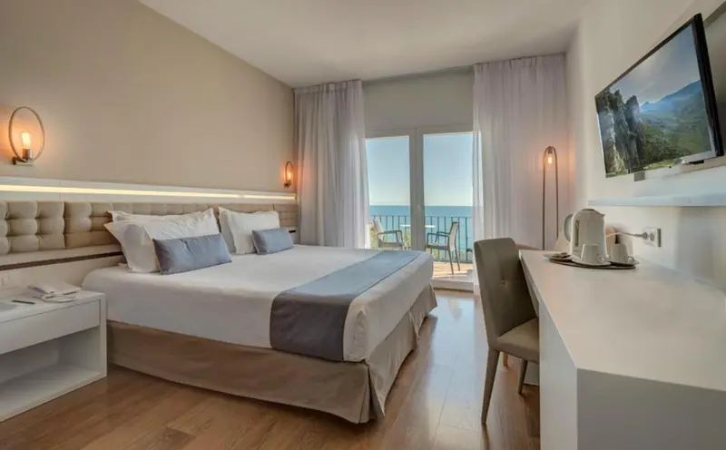 Chambre lumineuse avec un grand lit et une vue sur la mer.