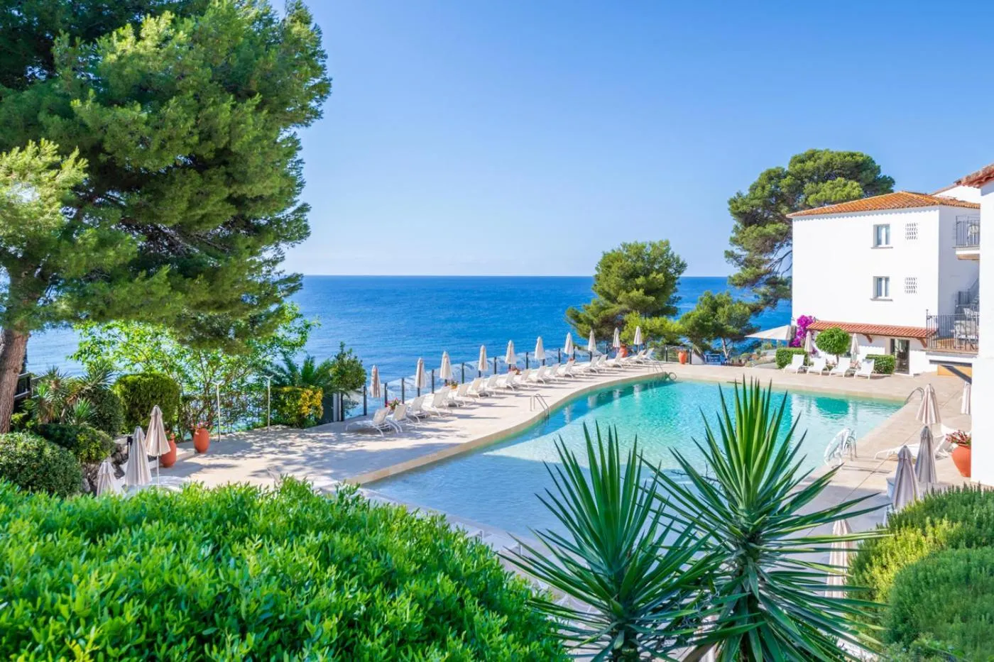 Une piscine rectangulaire bordée de transats et de parasols, avec vue sur la mer.