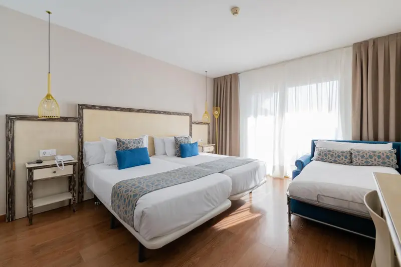 Une chambre lumineuse avec deux lits jumeaux et un canapé bleu.
