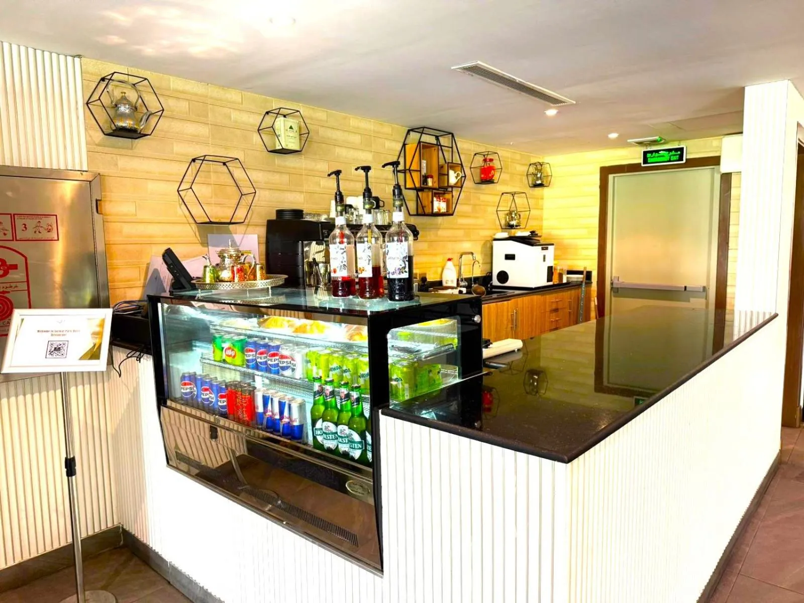 Un comptoir de bar avec des bouteilles et des boissons fraîches est présenté dans un espace lumineux.