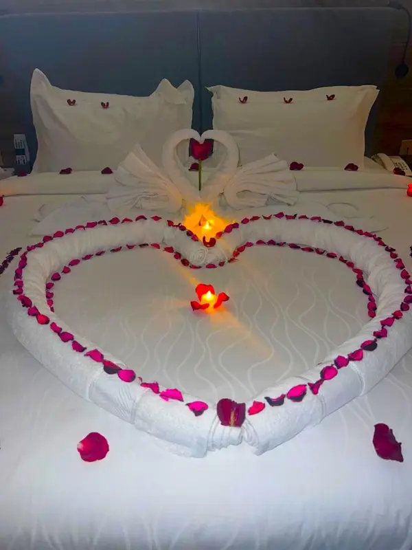 Lit double décoré de pétales de roses et de serviettes en forme de cœur, éclairé par des bougies.