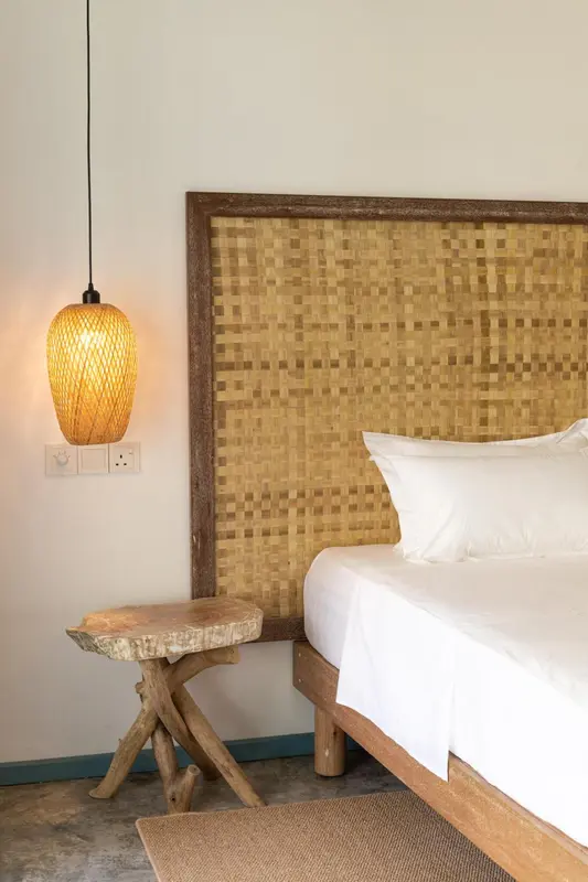 Une chambre lumineuse avec un lit recouvert de draps blancs et une tête de lit en bambou.