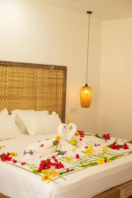 Un lit décoré de fleurs et de serviettes en forme de cygnes dans une chambre lumineuse.